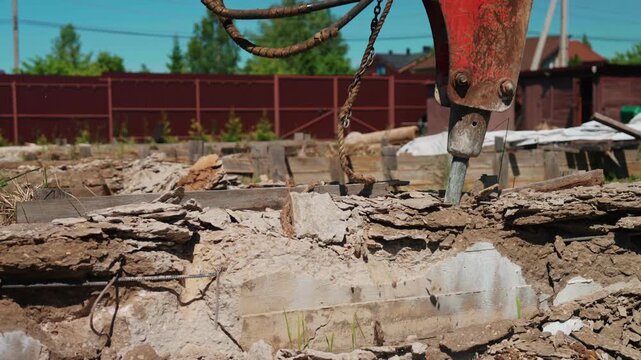Powerful hydraulic breaker smashing reinforced concrete slab during demolition work at a construction site, crushing the old building foundation into rubble with visible rebar and dust