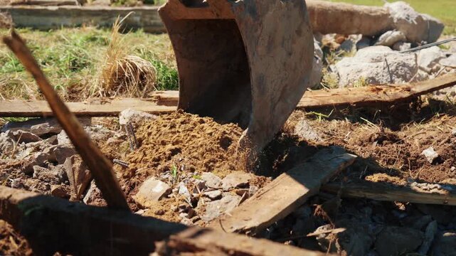 Heavy machinery excavator bucket digging a hole in the ground during construction work, moving earth, rubble, and soil on a sunny day. Industrial equipment operating at a building site