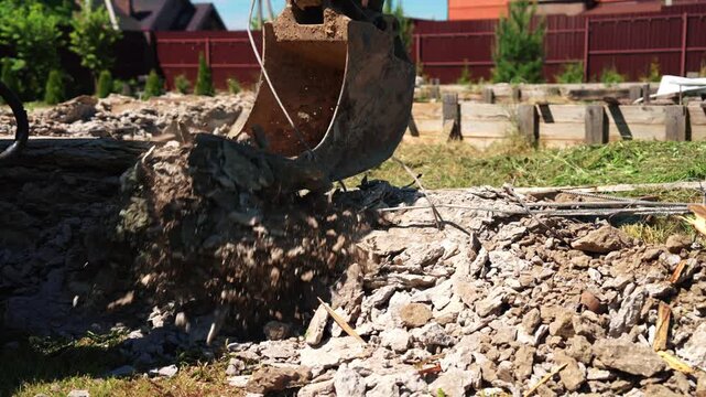 Industrial excavator bucket grabbing and moving broken concrete, rebar, and rubble during demolition work on a construction site, clearing the area for new building foundations