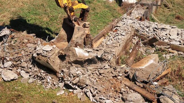 Heavy machinery breaking up and removing old concrete foundations from a construction site, crushing reinforced cement and clearing debris from the ground for new development on a sunny day