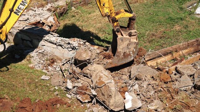 Heavy machinery with a powerful digging bucket breaking up old reinforced concrete and rubble during demolition work, clearing the ground on a construction site for new development