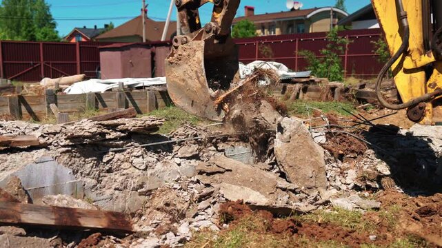 Heavy machinery dismantling an old reinforced concrete structure at a construction site. The digger's bucket breaks large concrete blocks into smaller pieces for removal during demolition