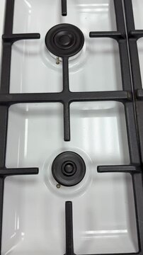 White gas stove cooktop closeup showing burner and black iron grate, glossy enamel surface with tiny droplets, low angle bottom