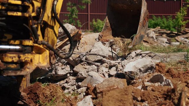Heavy machinery breaking reinforced concrete with a bucket during demolition work at a construction site. The powerful excavator arm crushes stone and rebar, clearing debris from the area