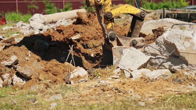 Heavy machinery excavating soil and concrete debris at a demolition area, with the hydraulic arm and bucket digging a ditch for foundation work during site preparation for a new building