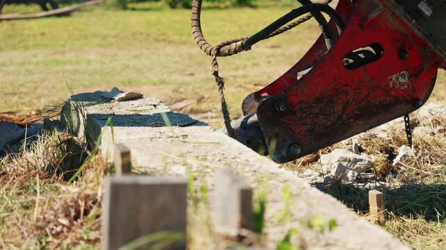 Close up of a powerful hydraulic jackhammer mounted on an excavator, breaking and crushing an old concrete curb during demolition work at a construction site on a sunny day
