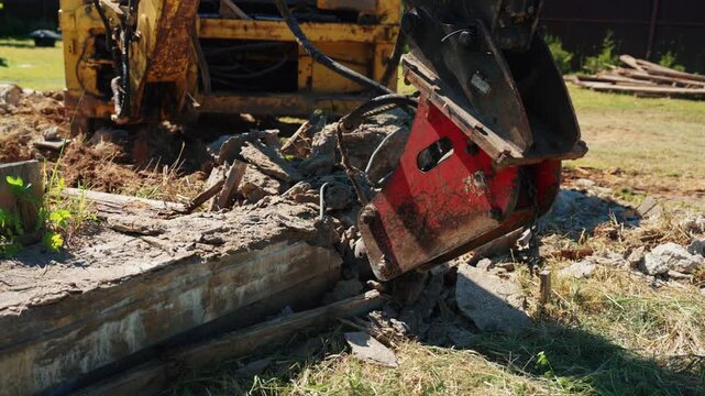 Powerful excavator with a hydraulic breaker attachment dismantling an old concrete block on a demolition site. Heavy machinery breaking reinforced concrete into smaller pieces for removal