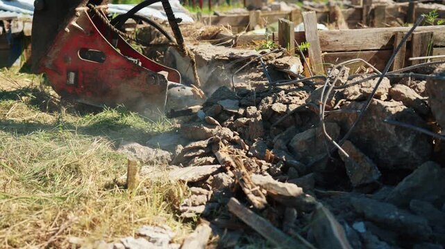 Close-up of a hydraulic breaker crushing concrete rubble with exposed reinforcing steel during residential foundation demolition, showing heavy equipment, structural removal and site cleanup.