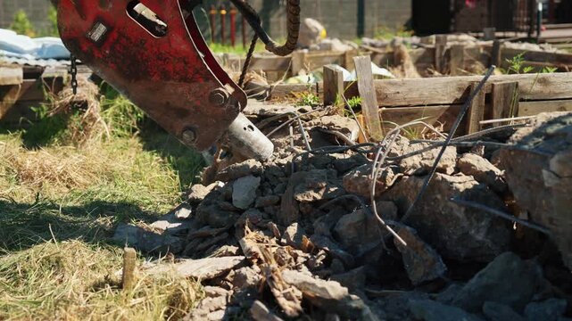 Powerful hydraulic hammer attachment breaking old reinforced concrete, crushing stones and rebar on a construction site. Heavy machinery dismantling a building foundation for a new development