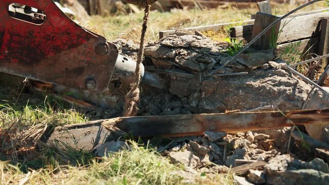 Close-up of a hydraulic breaker tearing reinforcing steel from broken concrete rubble during residential foundation demolition, showing structural removal, heavy equipment and site cleanup.