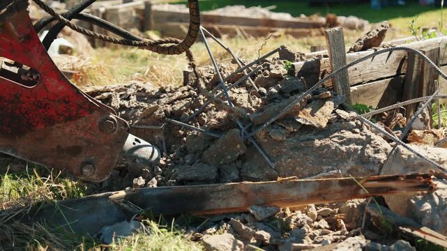 Heavy machinery with a hydraulic hammer breaking down an old reinforced concrete structure at a construction site, creating a pile of rubble, rebar, and debris during demolition work