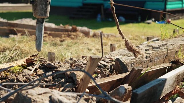 Close-up of a hydraulic breaker driving into a broken concrete foundation with twisted reinforcing steel and wooden formwork, showing residential demolition, structural removal and site cleanup.