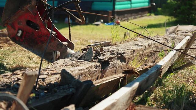 Heavy machinery with a hydraulic hammer breaking a reinforced concrete beam at a construction site. Professional demolition equipment dismantling an old building foundation on a sunny day