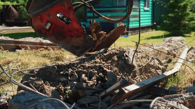 Close-up of a hydraulic breaker pulling twisted reinforcing steel from broken concrete debris during residential foundation demolition, showing structural removal, heavy equipment and site cleanup.