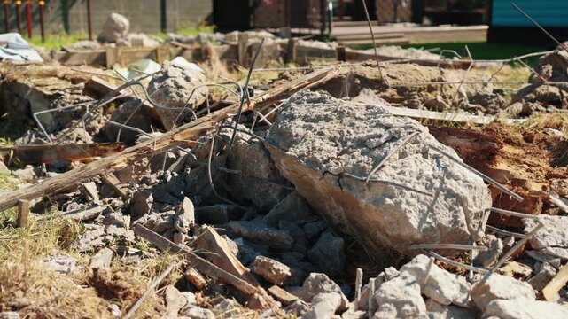 Broken reinforced concrete slabs and twisted rebar scattered across a demolition site, showcasing the aftermath of building destruction and site clearing for new construction on a sunny day