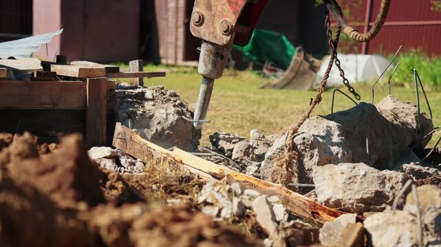 Powerful excavator with a hydraulic breaker attachment dismantling a reinforced concrete structure on a construction site, crushing stone and rebar with force and creating clouds of dust