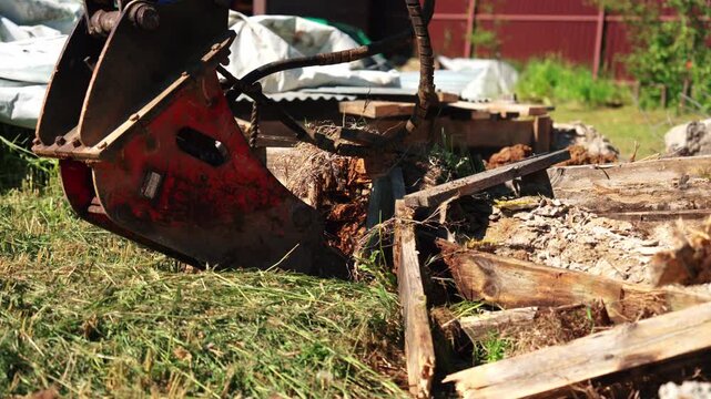 Low angle close-up of a backhoe loader bucket resting beside broken wooden formwork and foundation debris during residential demolition, showing heavy equipment and site cleanup.