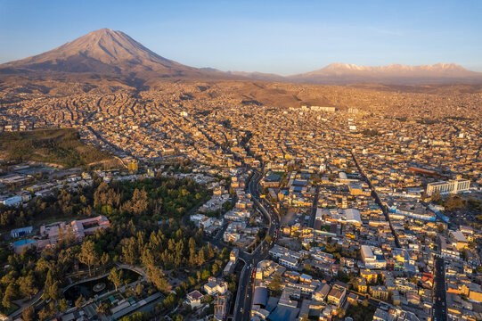 Aerial view of the Misti volcano towering over the dense urban landscape and historic rooftops of Arequipa during golden hour in Arequipa, Arequipa, Peru.