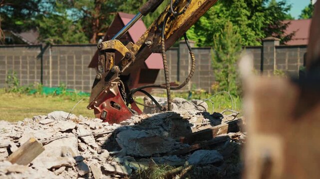 Low angle close-up of a hydraulic breaker resting above broken concrete foundation rubble during residential demolition, showing heavy equipment, structural removal and site preparation.