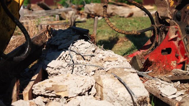 Close-up of a hydraulic breaker hovering above broken reinforced concrete foundation rubble with exposed twisted rebar during residential demolition, showing structural removal and site cleanup.