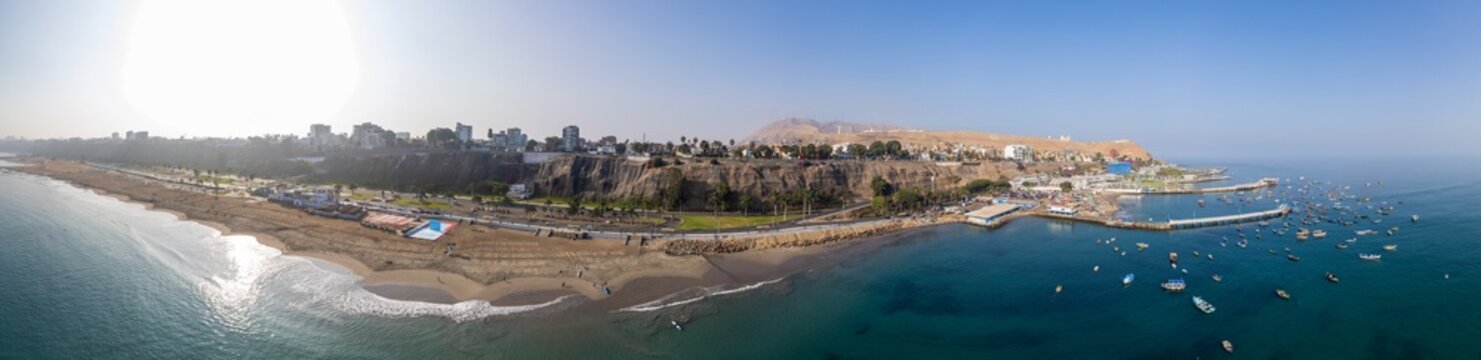 Aerial view of Malecon de Chorrillos featuring the coastal cliffs, sandy beach, and numerous small fishing boats anchored in the bay in Lima, Provincia de Lima, Peru.