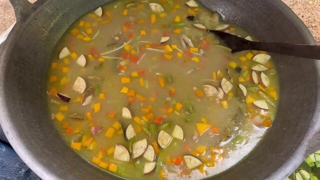 The initial stage of making *Asyura* porridge involves mixing all the ingredients and spices in a large wok and stirring the mixture continuously.