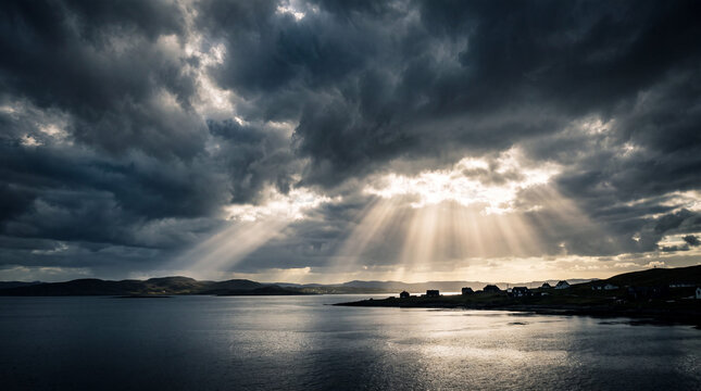 Dramatic sun rays breaking through dark storm clouds over a calm coastal landscape with small houses and mountains in the distance at twilight