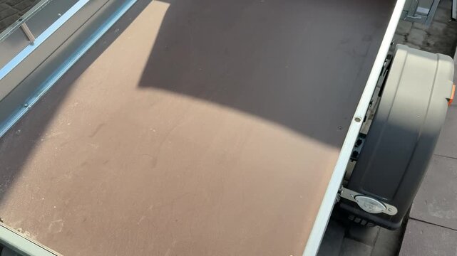 Top view empty trailer bed showing green metal frame and worn plywood floor with edge chips and small damage, sunlight casting