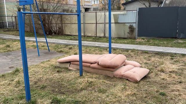 Courtyard pullup bar with sofa mats, spring day blue metal turnstile, stacked pink cushions from old sofa tossed on grass