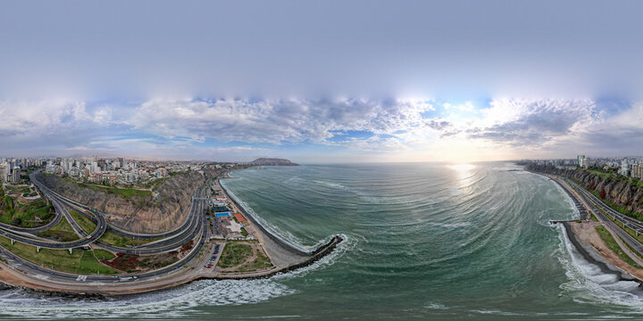 Aerial view of Costa Verde coastline featuring a winding highway along steep cliffs, urban buildings, and the Pacific Ocean under a cloudy sky in Miraflores, Provincia de Lima, Peru.