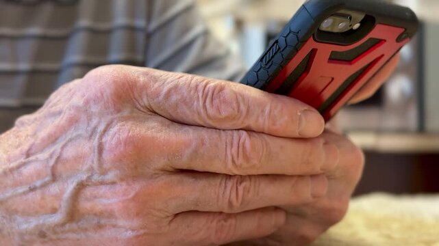 Elderly hands holding smartphone close-up, reading news on screen, large veins and wrinkled skin in sharp detail, sitting