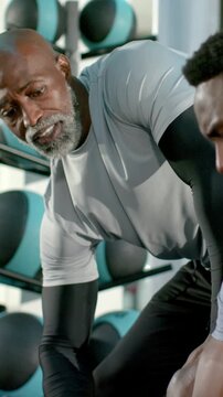 Vertical video: Leaning coach giving fist cues, counting client curling dumbbell in sleeves at gym
