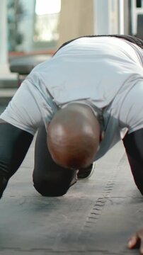 Vertical video: Kneeling man lowering chest to mat seam in gym, wearing workout top for strength