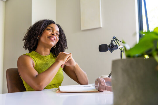 African American woman recording at desk in home studio wearing lime-green sleeveless top with mic