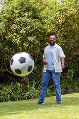 Naklejka premium African man standing smiling on lawn near shrubs watching soccer ball, wearing sneakers, copy space