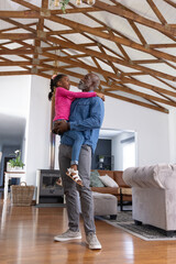 Naklejka premium African American family man holding child girl, smiling in living room with fireplace, wooden beams