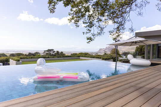 Translucent lounger is floating in infinity pool by wooden deck, with pink yellow strips