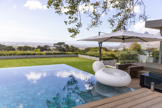 White ring lounge floating on infinity pool ledge under umbrella by wooden deck, reflecting sky
