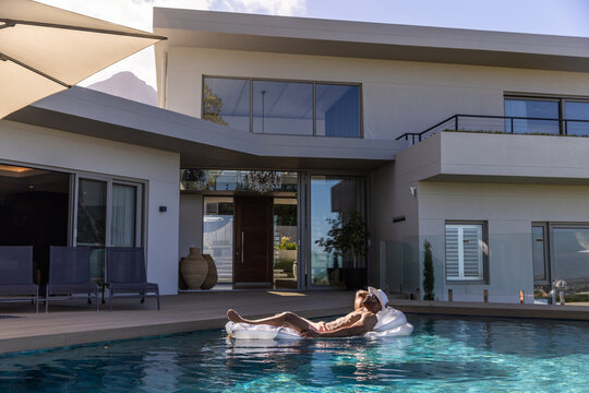 African American man lounging on clear float in briefs, wearing cap, sunglasses by pool, copy space