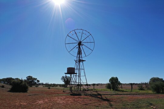 Aerial view of a classic metal windmill standing in the arid outback landscape under a bright sun in Barcaldine, Queensland, Australia.