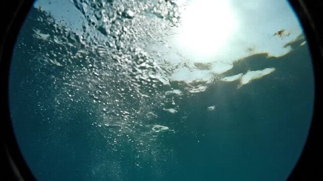 Underwater perspective showing sunlight rays penetrating the surface of the sea with oxygen bubbles rising through the clear blue ocean water depth