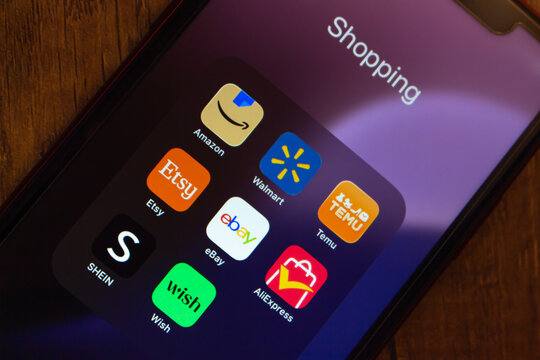 Mexico City, MEXICO - Jun 25 2026 : Smartphone displaying an e-commerce app icons including Amazon, Walmart, Etsy, eBay, Temu, SHEIN, AliExpress, and Wish on a dark wooden surface.