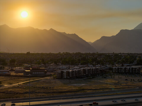 Aerial view of Lehi nestled against the Wasatch Range mountains during a hazy sunrise, with golden light illuminating the urban landscape and highway Lehi, Utah, United States.