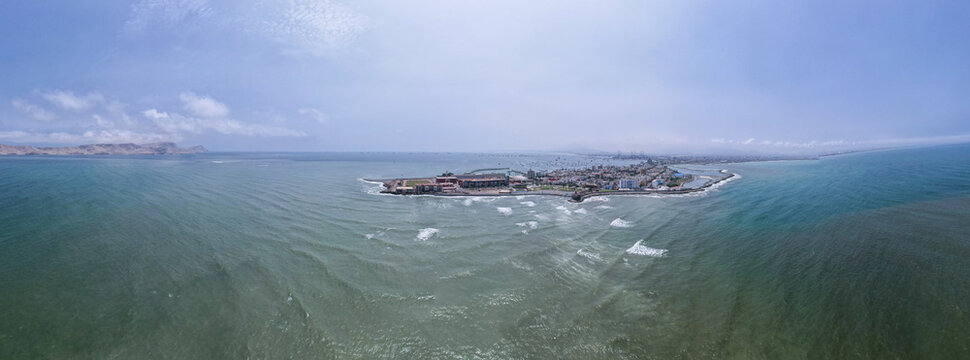 Aerial view of the La Punta peninsula, a coastal district surrounded by the Pacific Ocean, featuring urban buildings and a small harbor in La Punta, Callao Region, Peru.