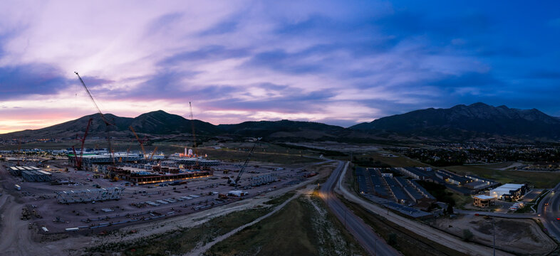 Aerial view of the Silicon Slopes construction site featuring cranes and heavy machinery set against the backdrop of Utah Valley and mountains at twilight in Lehi, Utah, United States.