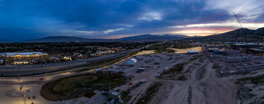 Aerial view of Silicon Slopes at twilight with construction sites, illuminated roads, and distant mountains under a dramatic sunset sky in Lehi, Utah, United States.