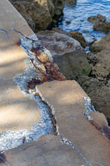 Fototapeta premium High angle view of severely cracked and spalling concrete seawall with rust stains and exposed aggregate next to rocky ocean shore