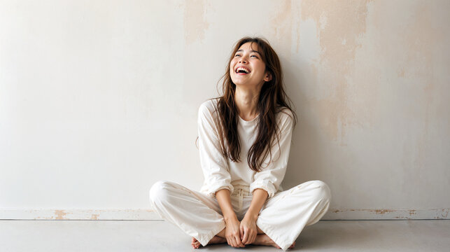 白い壁の前に座り笑う健康的な女性