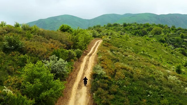 A man on a motorcycle rides off-road in a mountainous area with different vegetation. Daylight saving time.