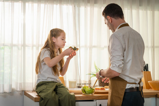 Family time cooking concept with dad and daughter in domestic kitchen, Father and daughter preparing healthy food together in modern kitchen, Happy young girl helping father cook meal at home
